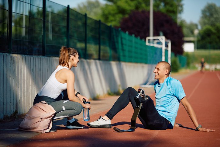 Happy athletic friends communicating while taking a break during sports training outdoors. Male athlete has prosthetic leg.